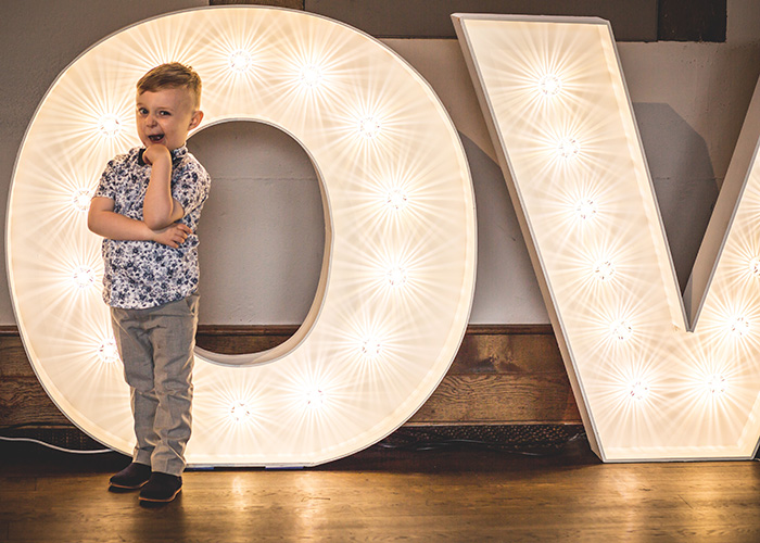 little boy standing in front of wedding light up letters