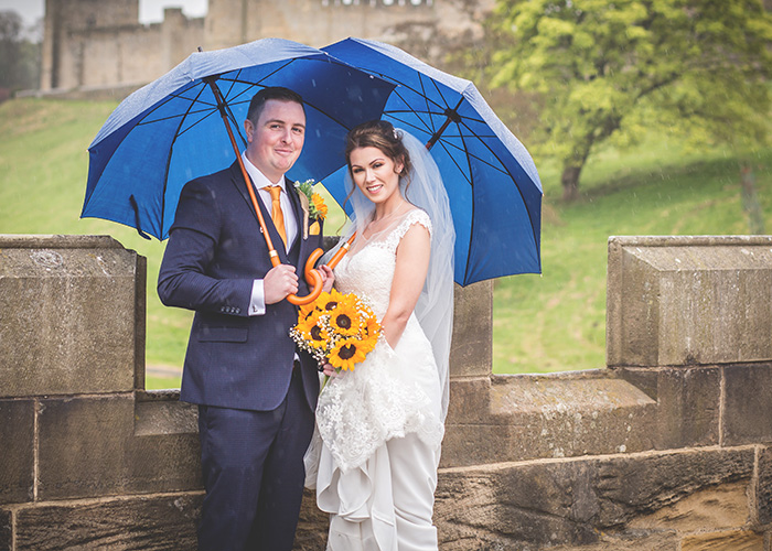 bride and groom with umbreallas on bridge